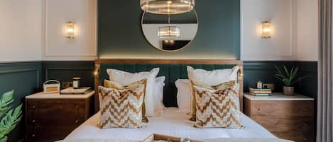 A bedroom with a large bed, two bedside tables, a mirror above the bed, and a chandelier.