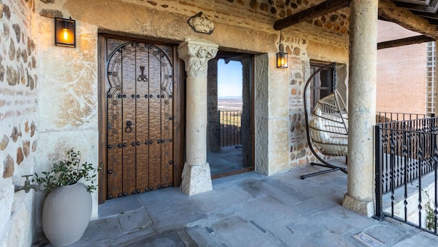 A stone facade with a wooden door and a large potted plant. - Mansion 35min Madrid|Cinema| Pool|BBQ| Car Charger (Guadalajara)