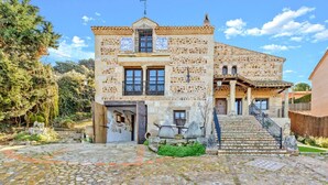 A stone building with a tiled roof, a balcony, and a staircase leading to the entrance. - Mansion 35min Madrid|Cinema| Pool|BBQ| Car Charger (Guadalajara)