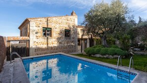 A stone building with a swimming pool, surrounded by greenery and a clear sky. - Mansion 35min Madrid|Cinema| Pool|BBQ| Car Charger (Guadalajara)