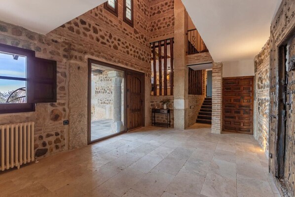Un interior espacioso con paredes de piedra, un amplio ventanal corredera y una escalera que conduce a un nivel superior.