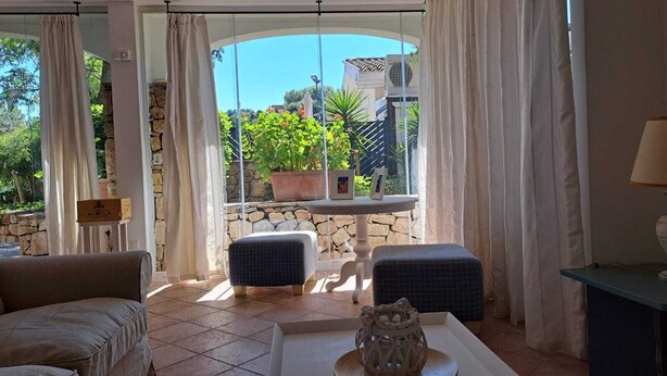 A sunlit room with a stone wall, a table with a vase, and a sofa.