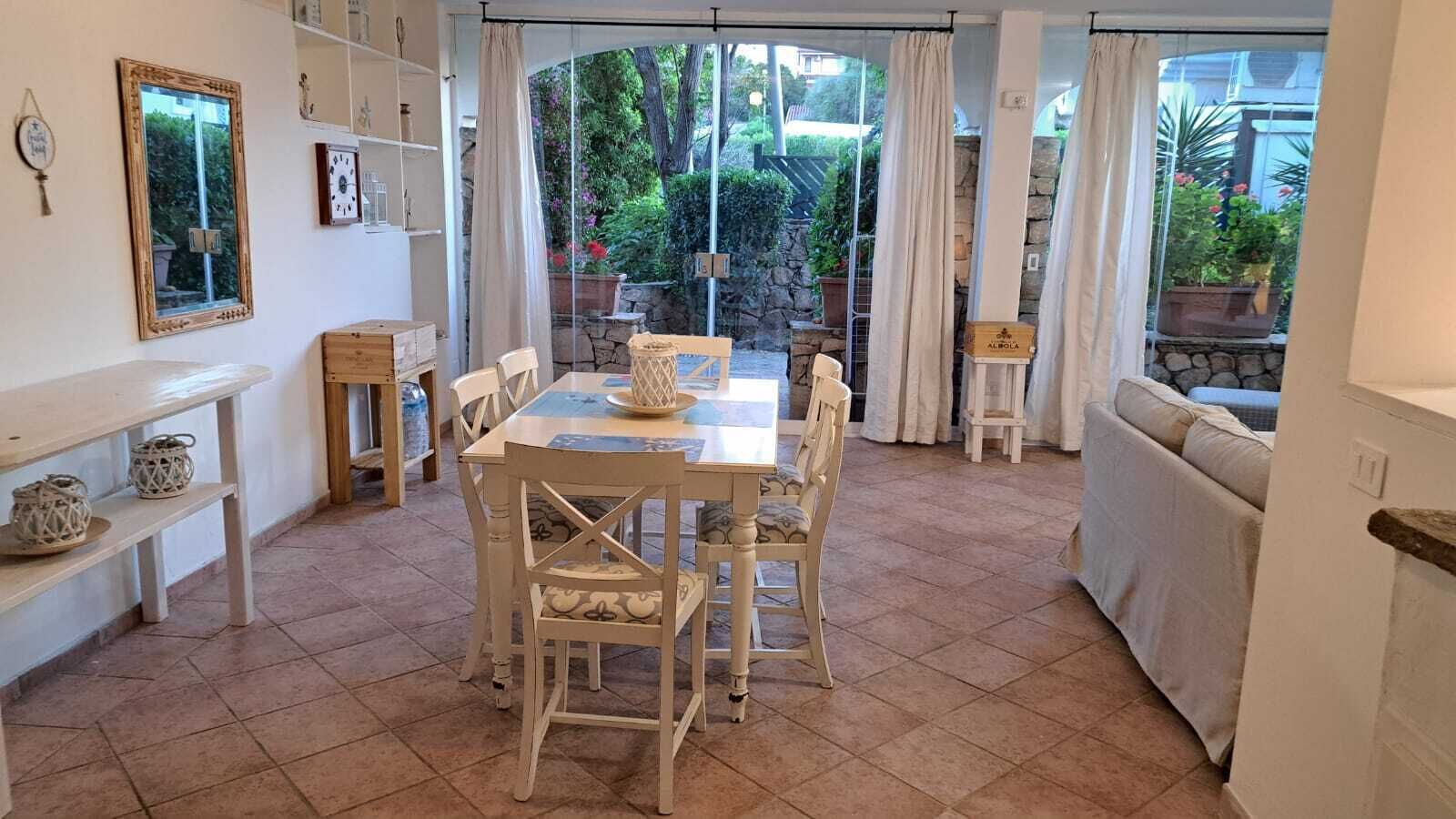 Un comedor con mesa y sillas, un espejo y vistas al jardín a través de amplios ventanales.