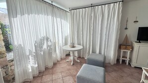 A room with a white table, two grey cushioned chairs, a white cabinet, and a TV on a stand.