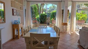 A sunlit patio with a dining table and chairs, surrounded by stone walls and potted plants.