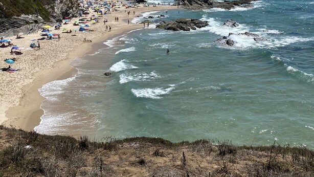 A beach with clear skies, rocky outcrops, and people enjoying the water. - Casa Alves (Palmela)