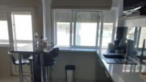 A modern kitchen with a dining area, large windows, and a trash bin. - Casa Alves (Palmela)