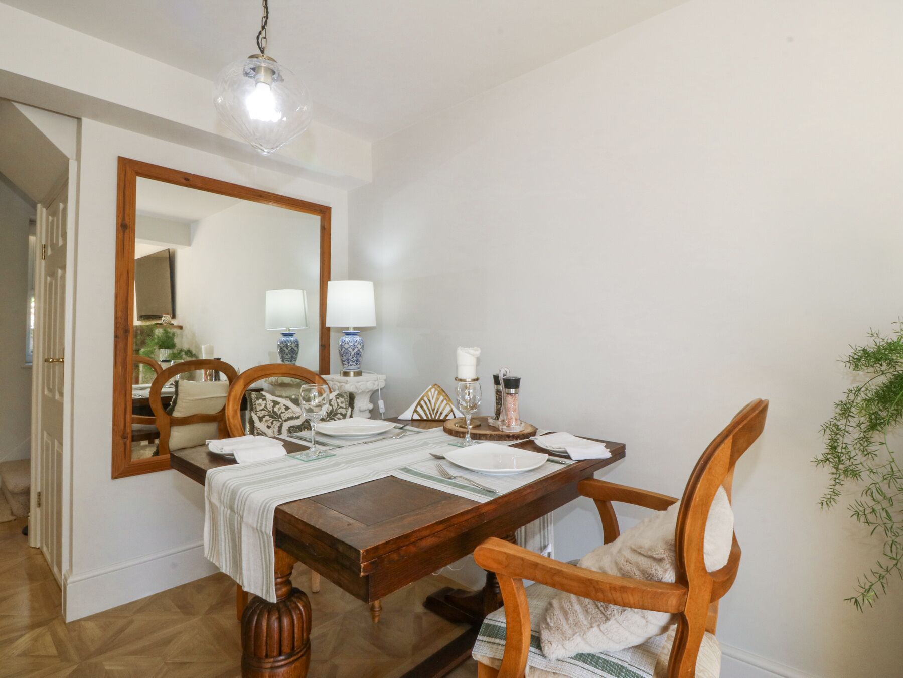 Un comedor con una mesa de madera, sillas, un espejo grande y una lámpara colgante.