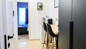 A modern kitchen with a dining area, a refrigerator, and a view into a bedroom.