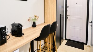 A compact kitchen with a wooden countertop, two black chairs, a black coffee machine, and a white refrigerator.
