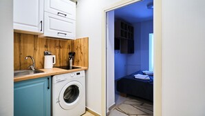 A compact kitchen with a washing machine, wooden countertop, and white cabinets.