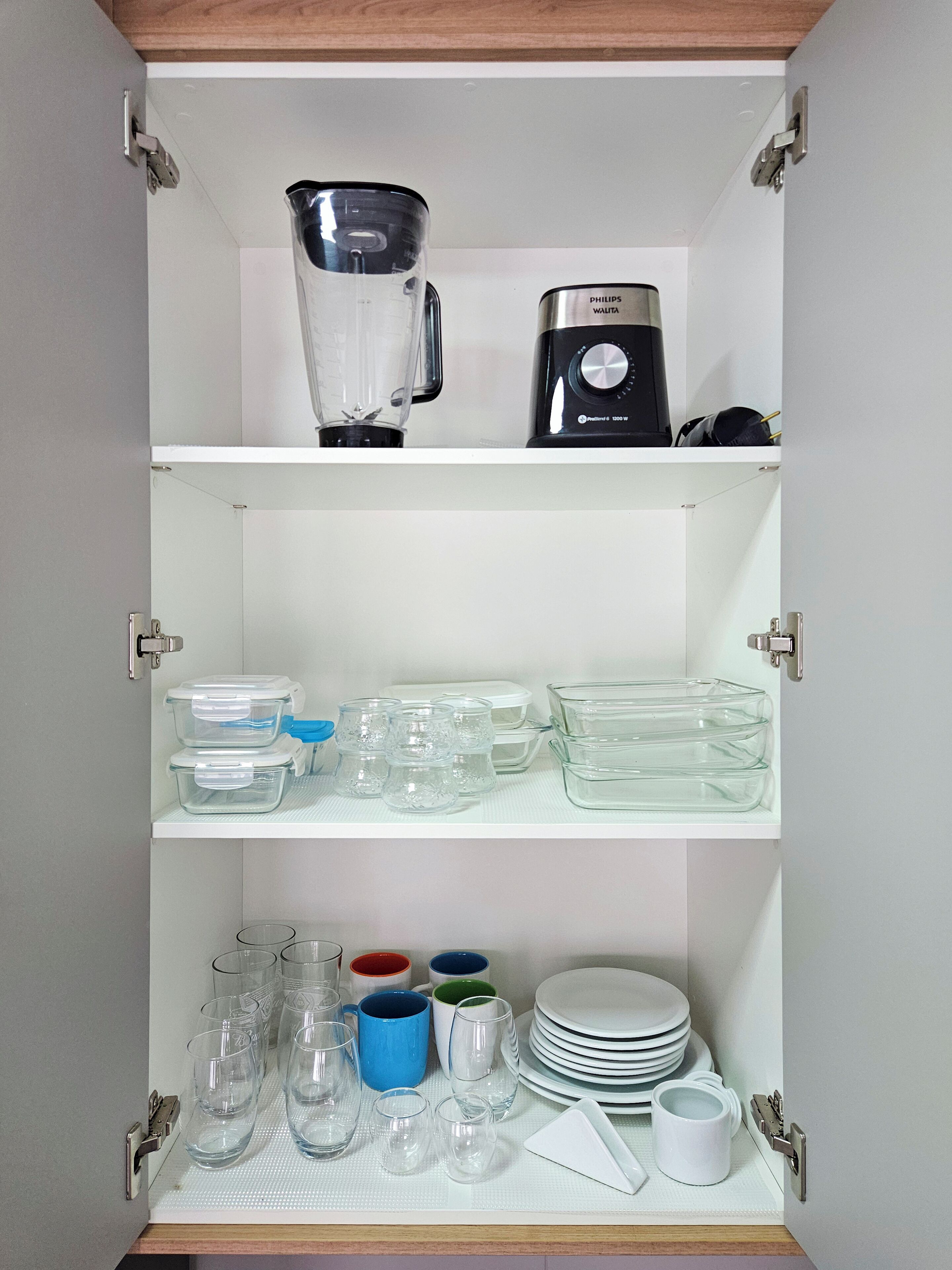 A kitchen cabinet with a blender, a coffee maker, and various glassware and dishes.