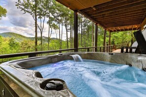 A hot tub with a waterfall feature, surrounded by a wooden deck and overlooking a forested landscape. - High Hopes by Mountain Oasis | Ellijay Cabin Hot Tub & Mountain Views (Ellijay)
