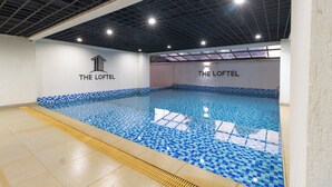 Una piscina interior con mosaicos azules, suelo de baldosas y techo con diseño de cuadrícula.