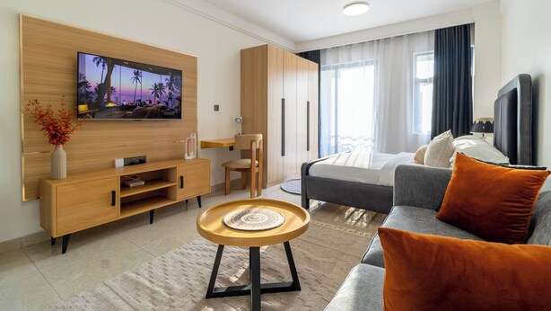 Una habitación de hotel moderna con un televisor montado en la pared, un sofá, una mesa de comedor y una silla.