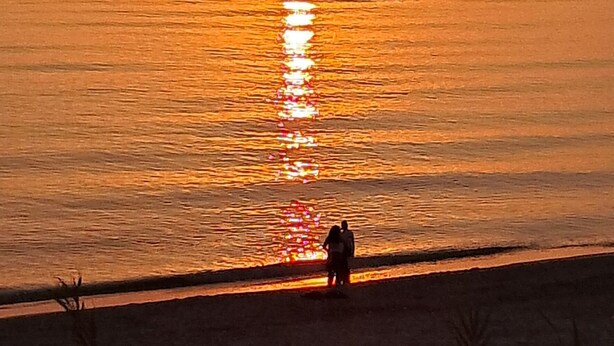 A sunset over a calm sea with a silhouette of two people on the shore.