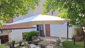 An outdoor patio area with a table and chairs, surrounded by greenery and a white umbrella.