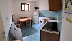 A compact kitchen with a dining table, a washing machine, a small refrigerator, and a sink.