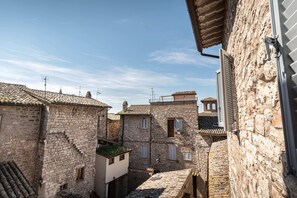 A narrow street with stone buildings, a small tower, and a clear sky. - B&B San Gabriele (Assisi)