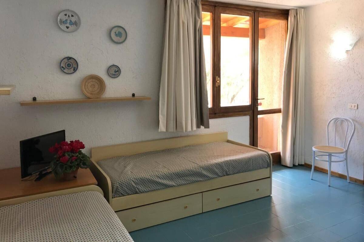 Une petite pièce agréable, dotée d’un lit simple, d’une table de chevet en bois, d’une chaise et d’une fenêtre avec des rideaux.