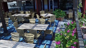 Ein Sitzbereich im Freien mit Tischen und Stühlen, der von einer Pergola überdacht und mit Kübelpflanzen und Blumen geschmückt ist.