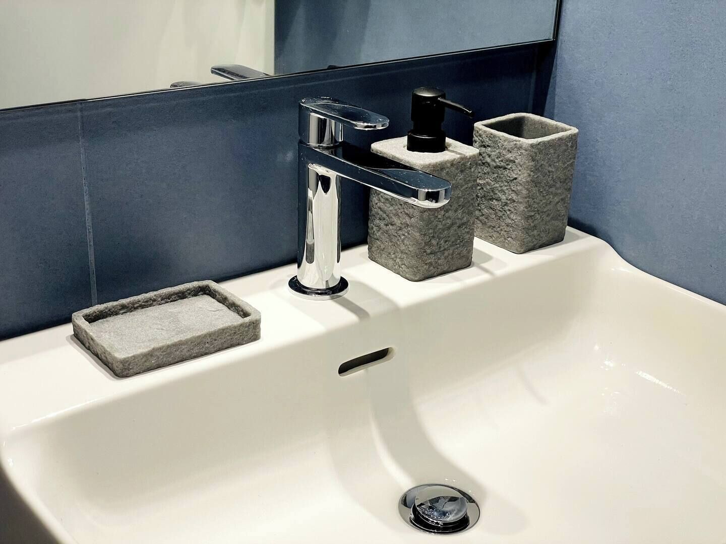 A white bathroom sink with a chrome faucet, a soap dish, and two stone soap holders.