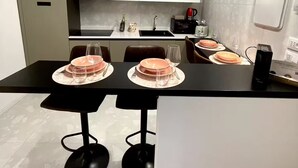 A modern kitchen with a dining table set for four, featuring a coffee machine, a kettle, and a wine bottle.