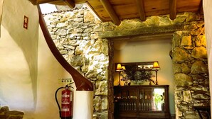Un intérieur aux murs de pierre, avec un extincteur, un escalier en bois et un banc.