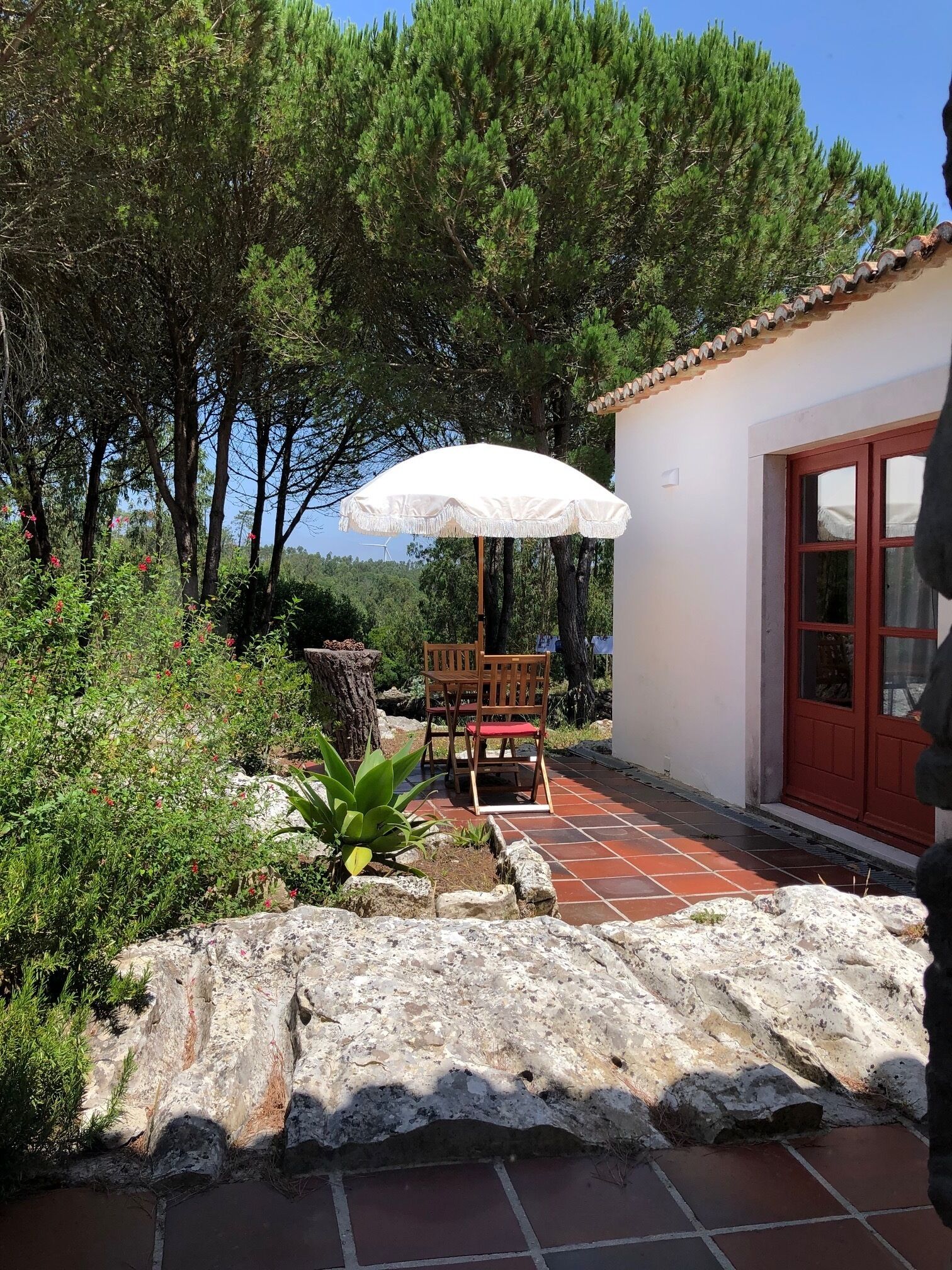 An outdoor patio with a white umbrella, a wooden table and chairs, and a stone wall.