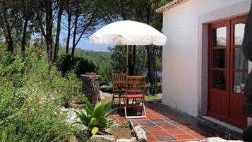 An outdoor patio with a white umbrella, a wooden table and chairs, and a stone wall.