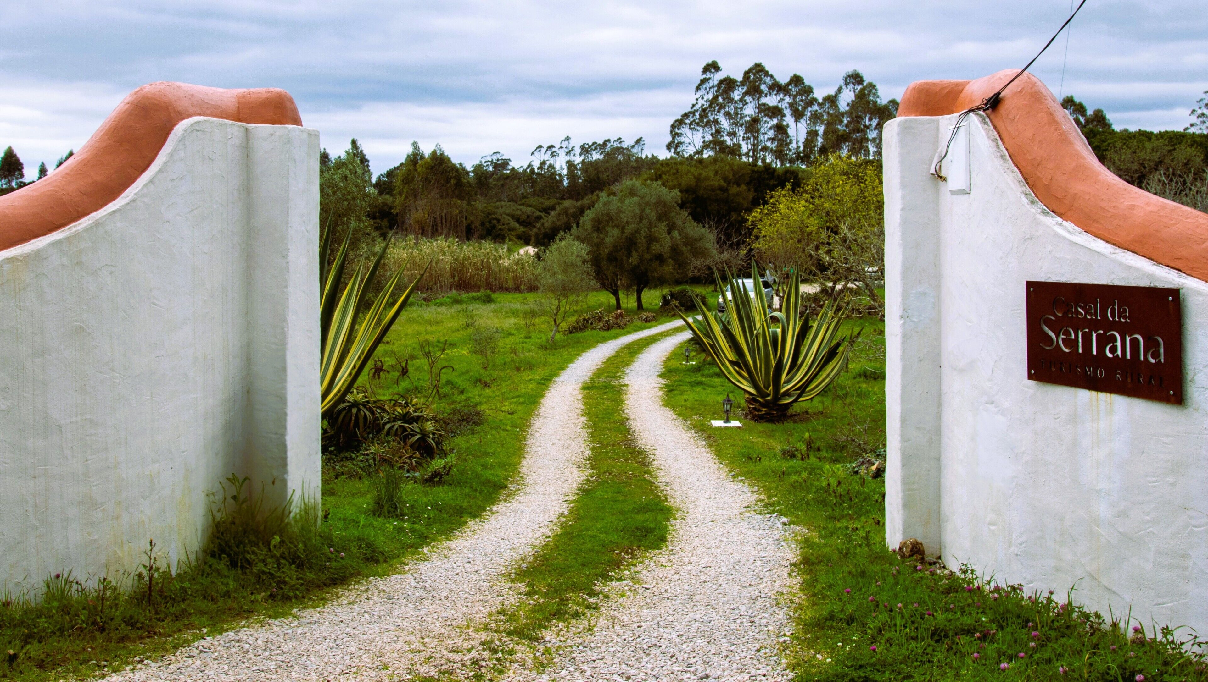 Un sendero de grava que conduce a una puerta con un cartel que dice 'Casal da Serrana'.