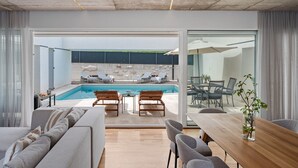 Ein modernes Wohnzimmer mit Pool, Essbereich und Küche, die durch Glastüren sichtbar sind.