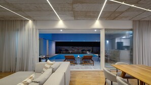 Ein modernes Wohnzimmer mit Sofa, Esstisch und Stühlen, das zu einem Poolbereich mit Liegestühlen führt.