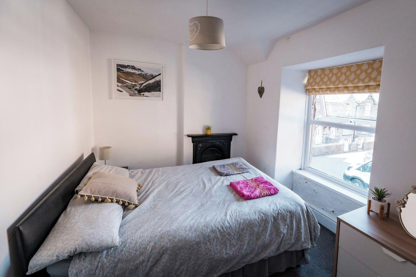 Un dormitorio con cama, ventana con vista a la calle, chimenea y una lámpara de pared.