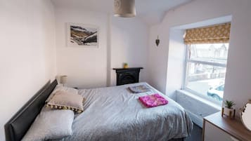 Un dormitorio con cama, ventana con vista a la calle, chimenea y una lámpara de pared.