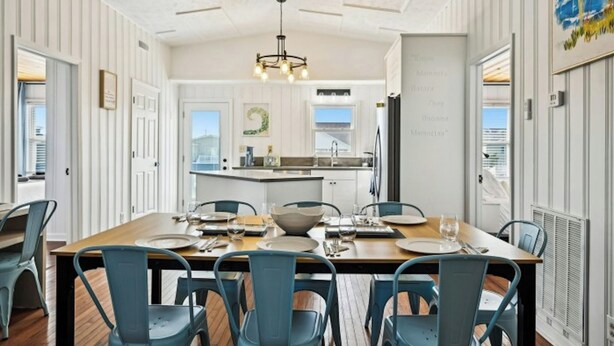 A dining area with a large wooden table set for six, surrounded by blue chairs. - Second Star- 7BR Channel House-Pool, Putting Green (North Myrtle Beach)