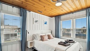 A bedroom with a wooden ceiling, a bed with white bedding, two pillows, a bedside table, and a window with curtains. - Second Star- 7BR Channel House-Pool, Putting Green (North Myrtle Beach)