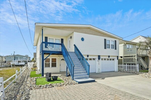 A two-story house with a blue staircase, a garage, and a front yard with a white picket fence. - Second Star- 7BR Channel House-Pool, Putting Green (North Myrtle Beach)