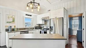 A modern kitchen with white cabinetry, a central island, stainless steel appliances, and a pendant light fixture. - Second Star- 7BR Channel House-Pool, Putting Green (North Myrtle Beach)