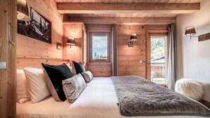 A wooden cabin bedroom with a bed, pillows, a fur throw, and two wall-mounted lamps. - Solstice - Spacious Alpine Apartment Les Gets (Les Gets)