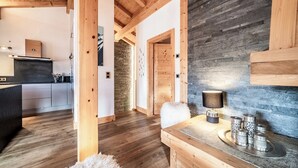 A modern kitchen with wooden beams, a stone wall, and a wooden dining table with decorative metalware. - Solstice - Spacious Alpine Apartment Les Gets (Les Gets)