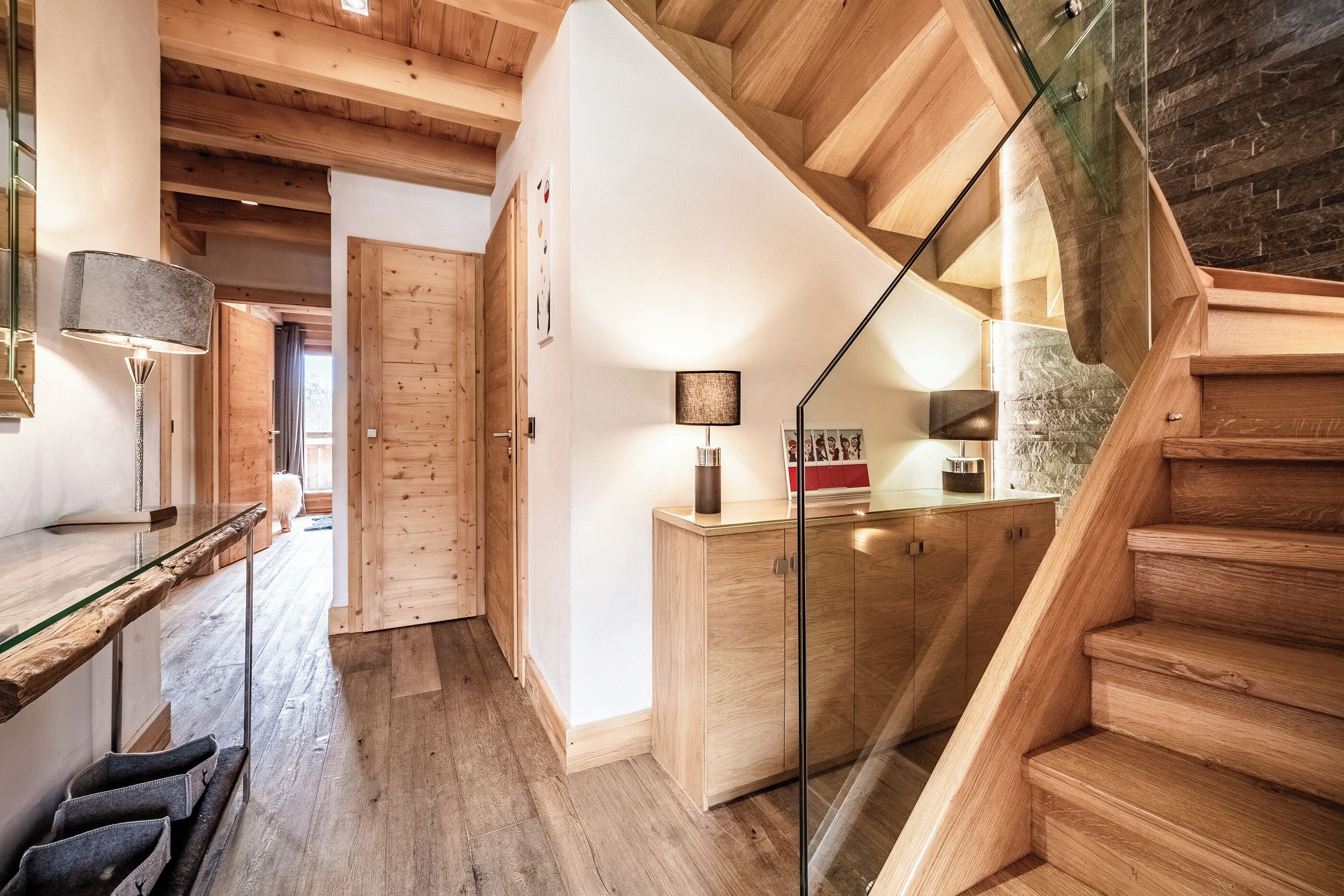 Un interior moderno con una escalera de madera, una puerta de cristal y una zona de cocina con armarios de madera.