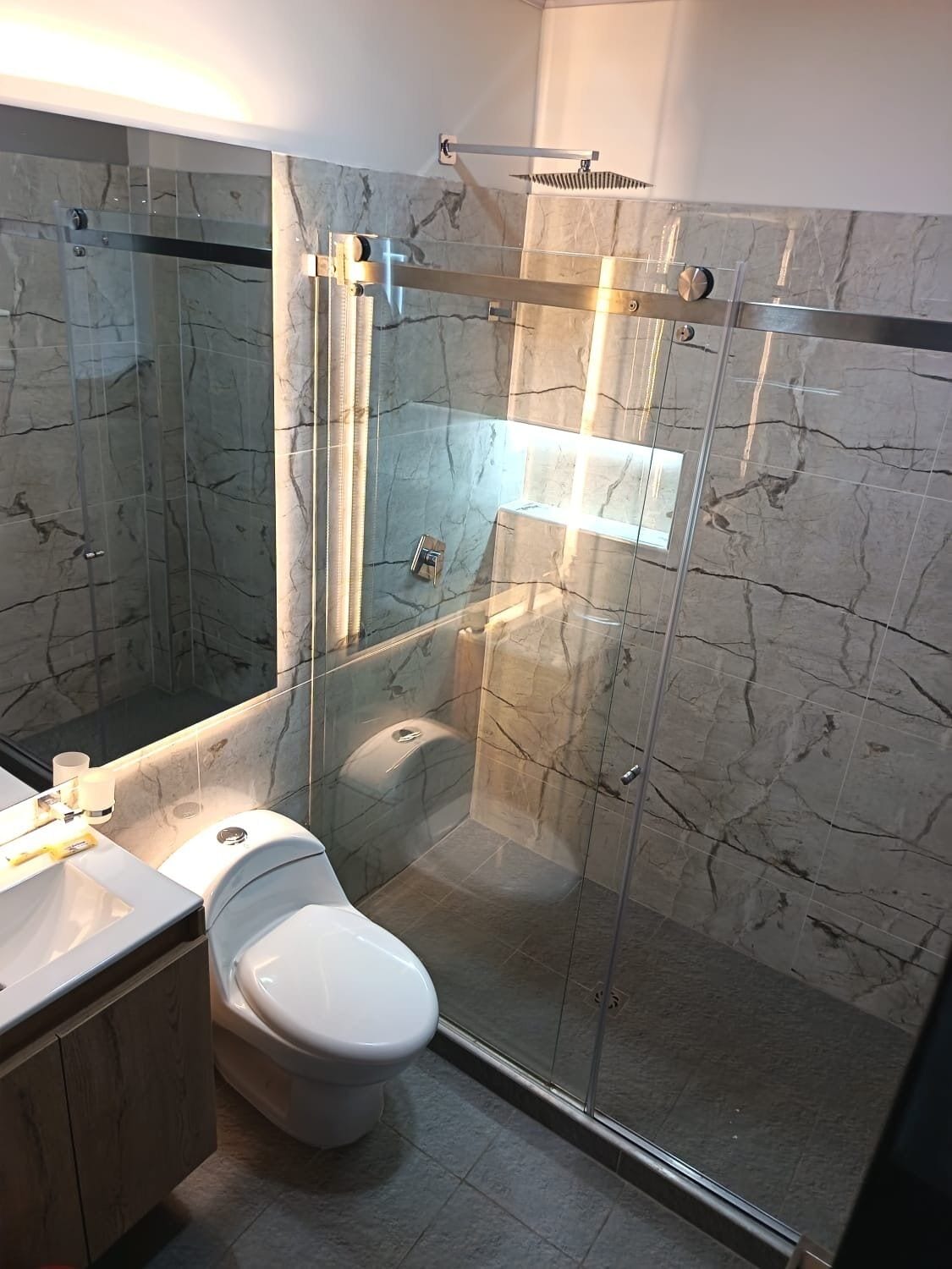 A modern bathroom with a glass-enclosed shower, a white toilet, and a marble-tiled wall.
