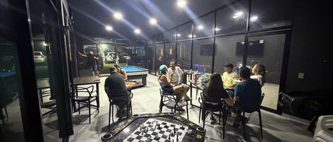 A group of people playing pool in a well-lit indoor space with a large pool table at the center.