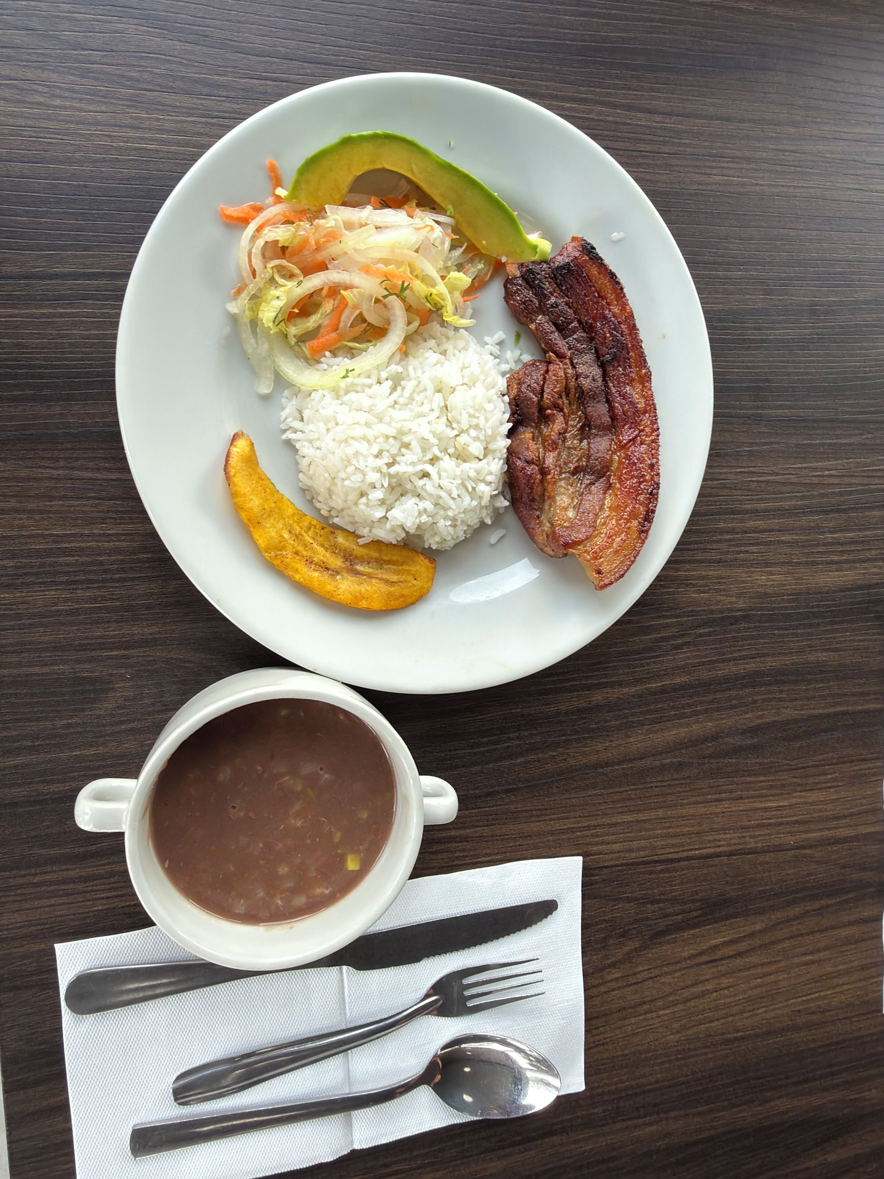 Un plato con arroz, una porción de carne, media aguacate y una ensalada al lado, sobre una mesa de madera.