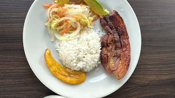 Un plato con arroz, una porción de carne, media aguacate y una ensalada al lado, sobre una mesa de madera.