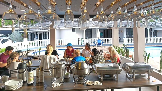 A covered outdoor dining area with tables, chairs, and hanging glass light fixtures.