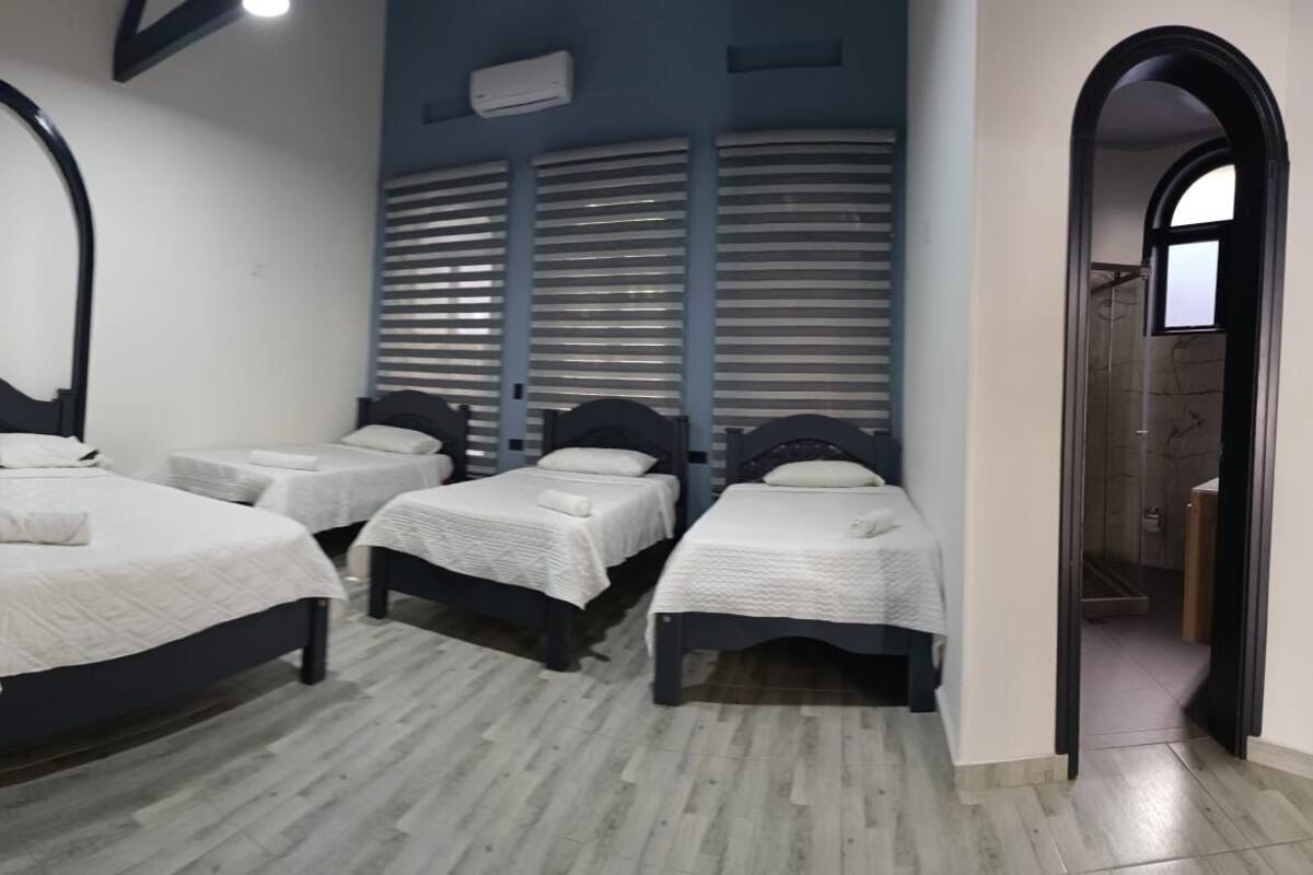 Une chambre d’hôtel avec trois lits, une petite table et un espace douche.
