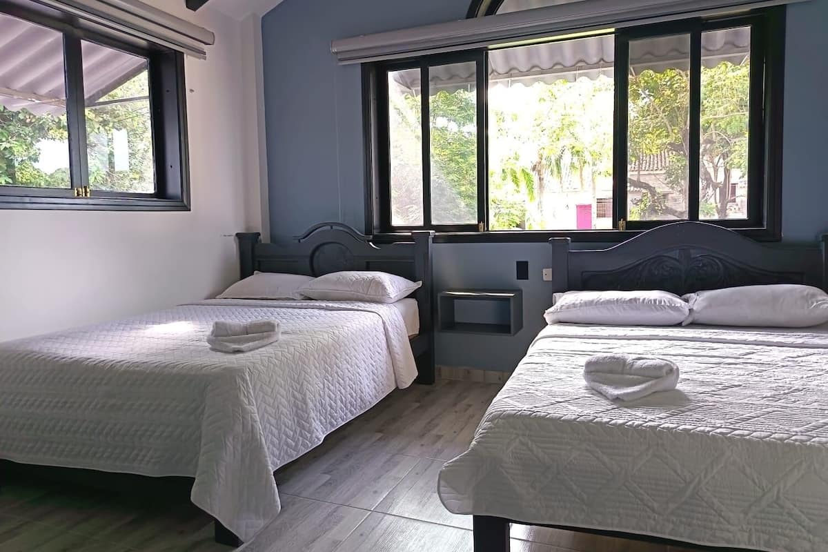Une chambre avec deux lits, une fenêtre donnant sur un espace verdoyant et un plafond doté d’une lucarne.
