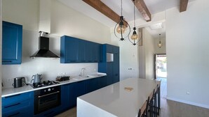A modern kitchen with blue cabinets, a white countertop, and a large island. There is a stove, sink, and a hanging light fixture. - VILLA ALTUN 1 (Mugla)